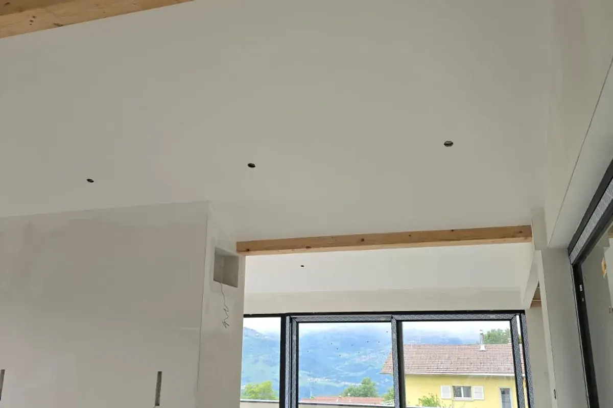 Séjour moderne fini, plafond et murs en plâtre blanc lissé, poutres apparentes, vue sur les montagnes du Valais